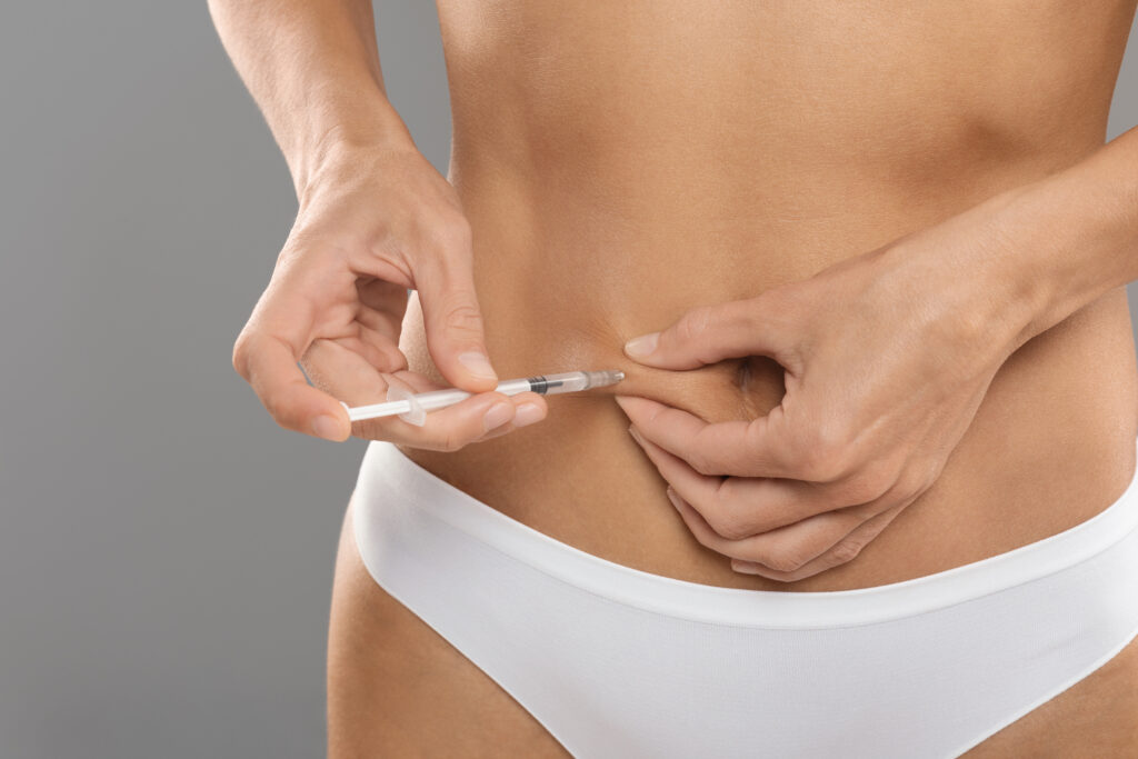 Mulher aplicando injeção na região abdominal, usando uma seringa fina e vestindo roupa íntima branca.