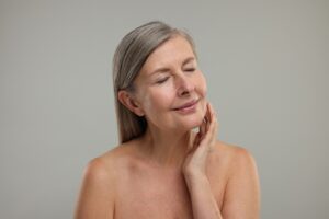 Uma mulher mais velha, com cabelos grisalhos, toca suavemente seu rosto com a mão, com os olhos fechados e uma expressão serena.