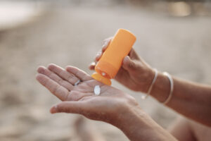 Mulher madura de cabelos grisalhos, olhos fechados, tocando o rosto com as mãos em gesto de cuidado com a pele, sobre fundo neutro.