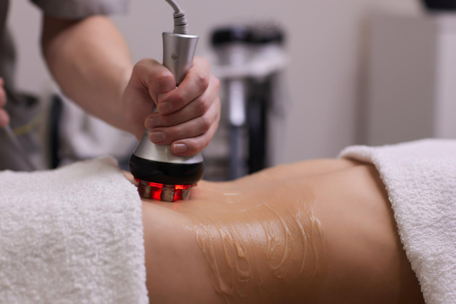 Pessoa recebendo tratamento estético de radiofrequência na região abdominal, com aplicação de gel condutor e uso de aparelho com luz vermelha