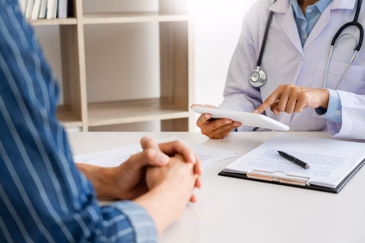Médico mostrando informações em um tablet para paciente durante consulta em consultório.