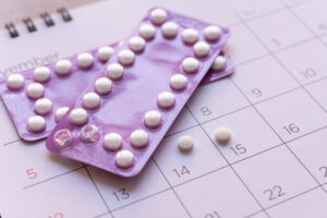 Cartelas de anticoncepcional com comprimidos sobre calendário mensal, indicando acompanhamento do ciclo e uso contínuo da medicação.