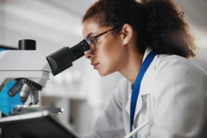 Profissional de laboratório utiliza um microscópio para analisar amostras em ambiente clínico ou de pesquisa.
